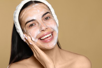 Photo of Happy young woman washing face with cosmetic product on beige background, closeup. Space for text