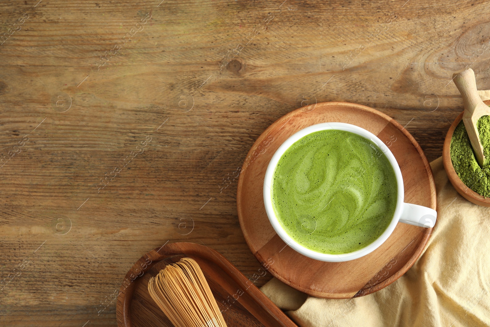 Photo of Cup of fresh matcha latte, powder and bamboo whisk on wooden table, flat lay. Space for text