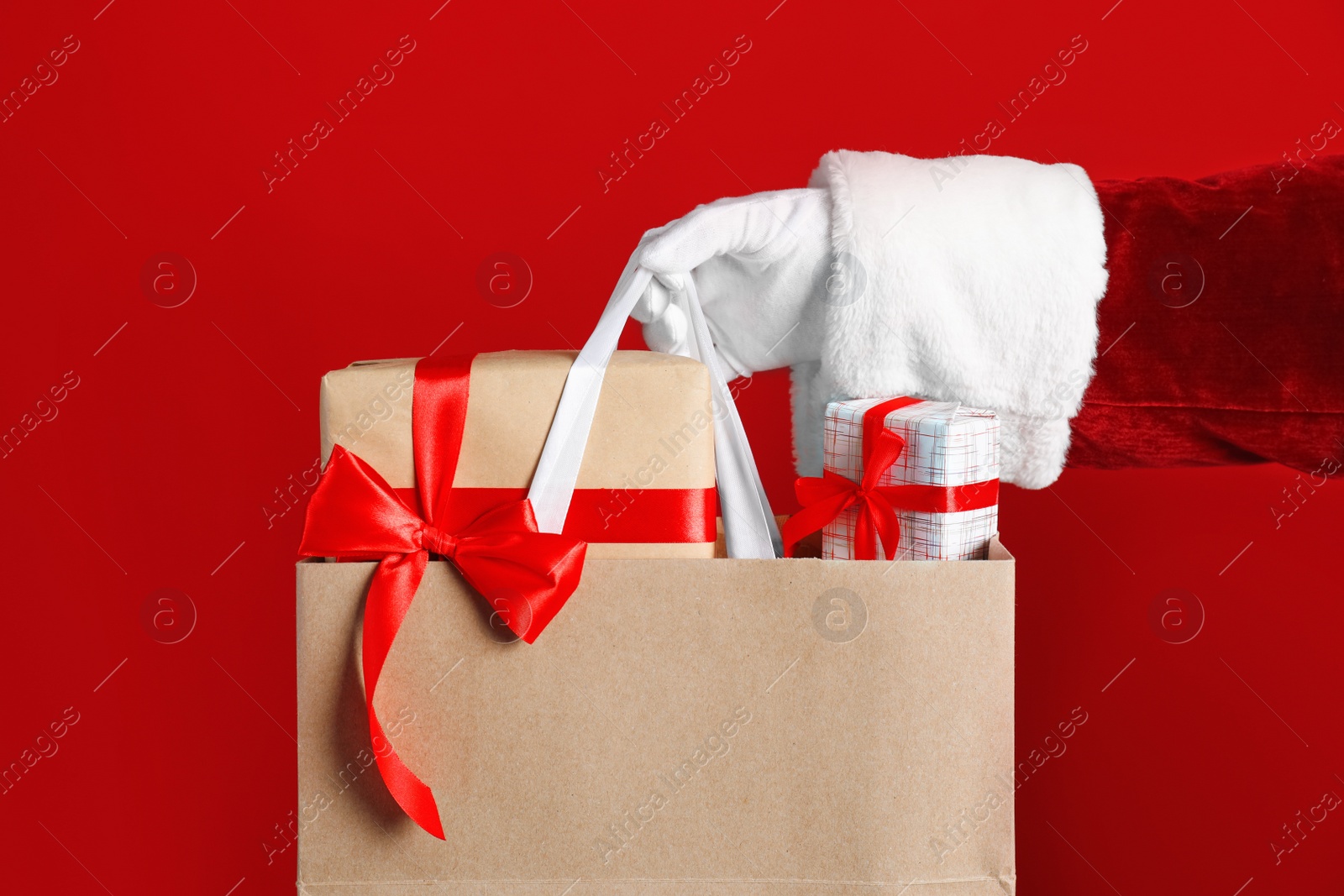 Photo of Santa holding paper bag with gift boxes on red background, closeup