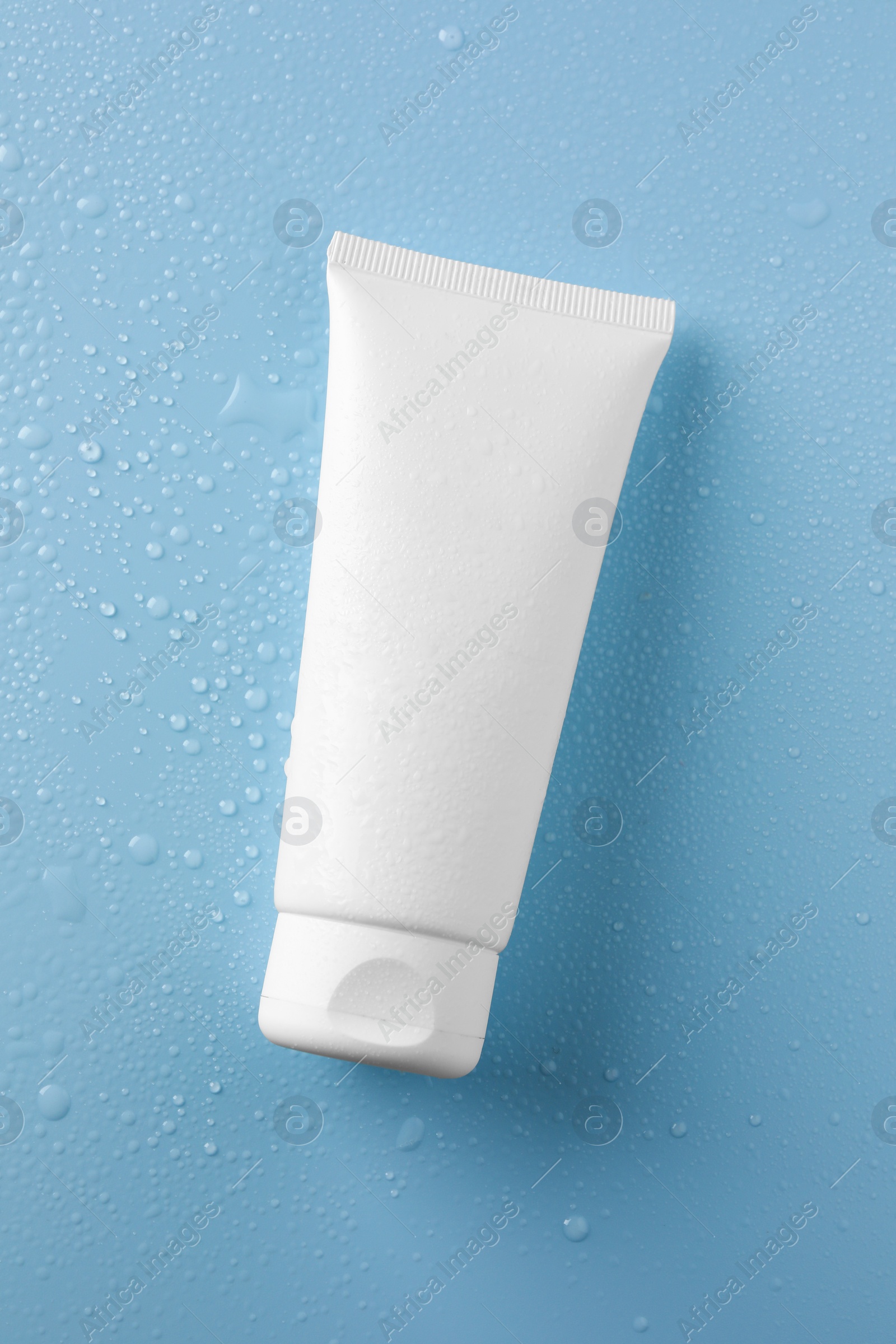 Photo of Moisturizing cream in tube on light blue background with water drops, top view