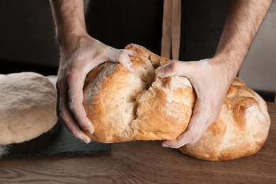 Photo of Male baker holding loaf of bread over table, closeup