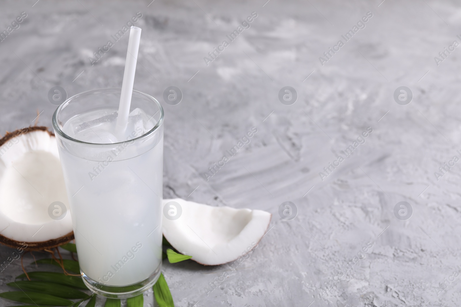 Photo of Glass of coconut water with ice cubes, palm leaf and nut on grey table. Space for text