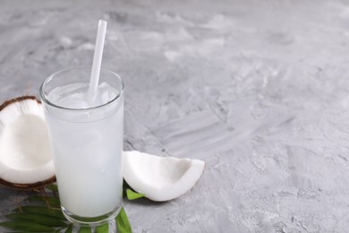 Photo of Glass of coconut water with ice cubes, palm leaf and nut on grey table. Space for text