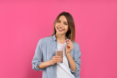 Young woman with glass of chocolate milk on pink background