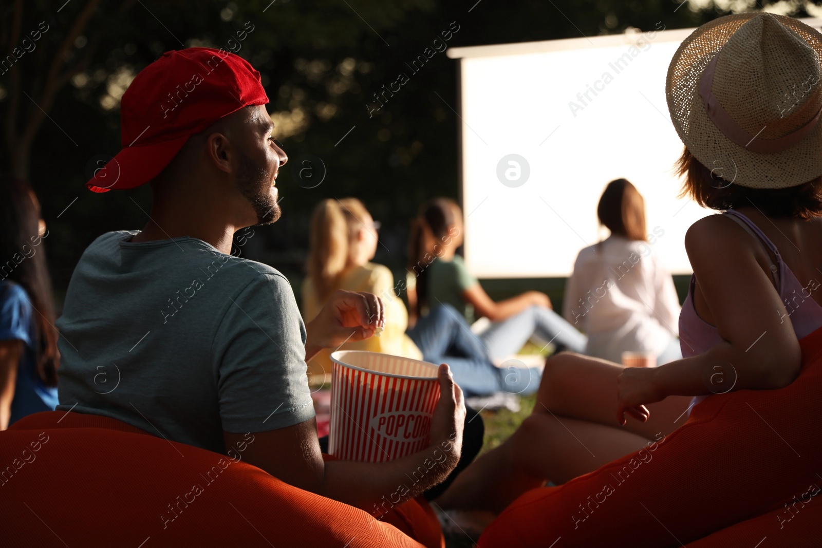 Photo of Young couple with popcorn watching movie in open air cinema. Space for text