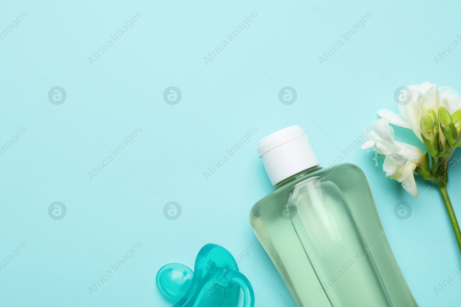 Photo of Bottle of baby oil, pacifier and blooming freesia on turquoise background, flat lay. Space for text