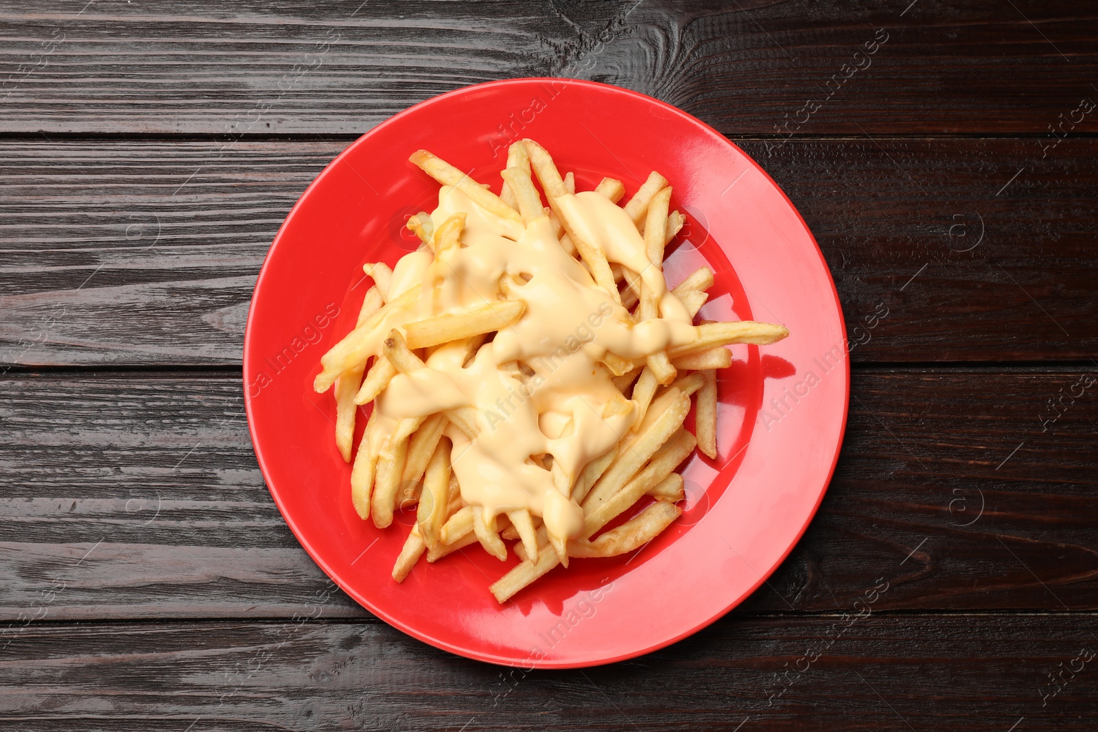 Photo of Delicious french fries with cheese sauce on wooden table, top view