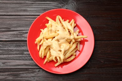 Delicious french fries with cheese sauce on wooden table, top view