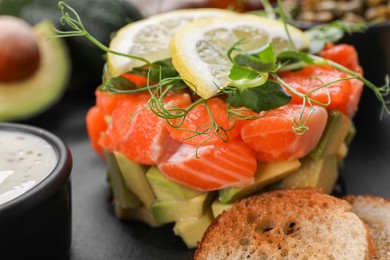 Delicious salmon tartare served with avocado, sauce and croutons on dark board, closeup