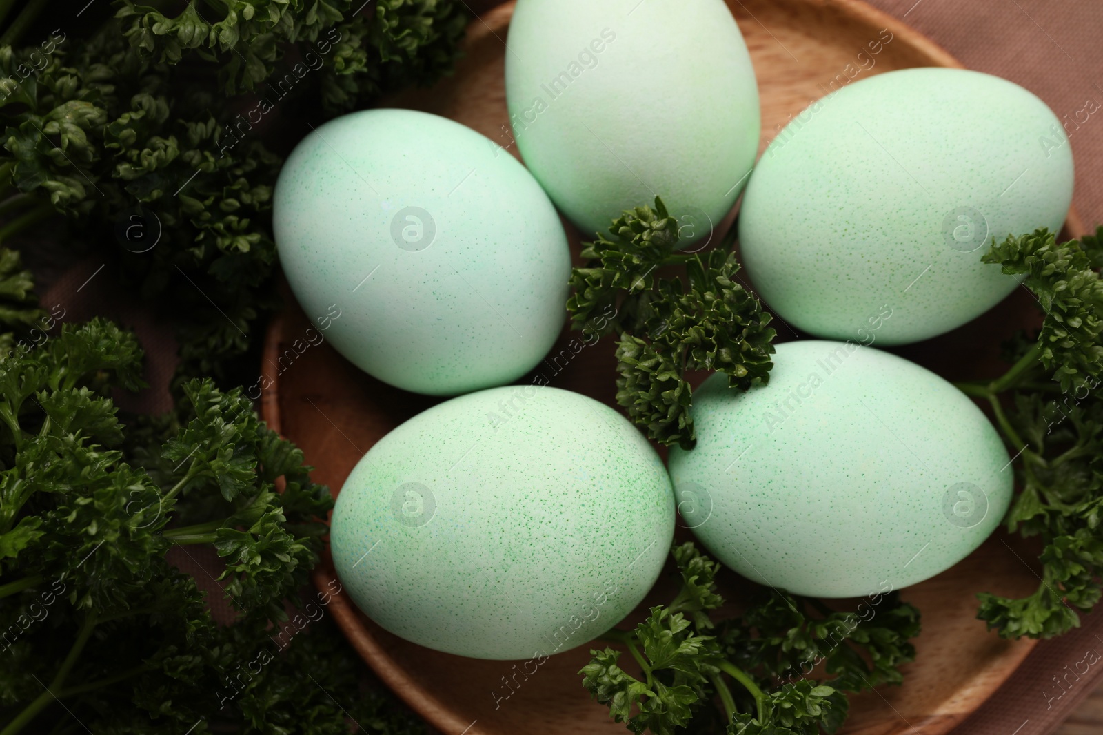 Photo of Turquoise Easter eggs painted with natural dye and curly parsley on table, flat lay