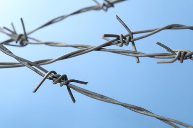 Metal barbed wire on light blue background, closeup