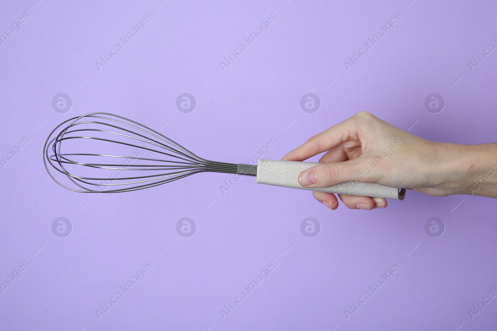 Photo of Woman holding metal whisk on lilac background, closeup