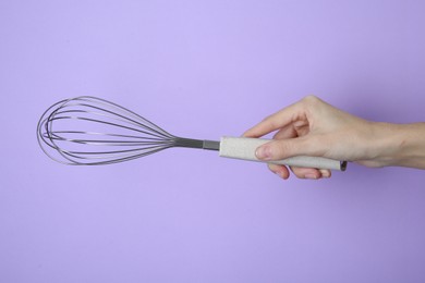 Woman holding metal whisk on lilac background, closeup