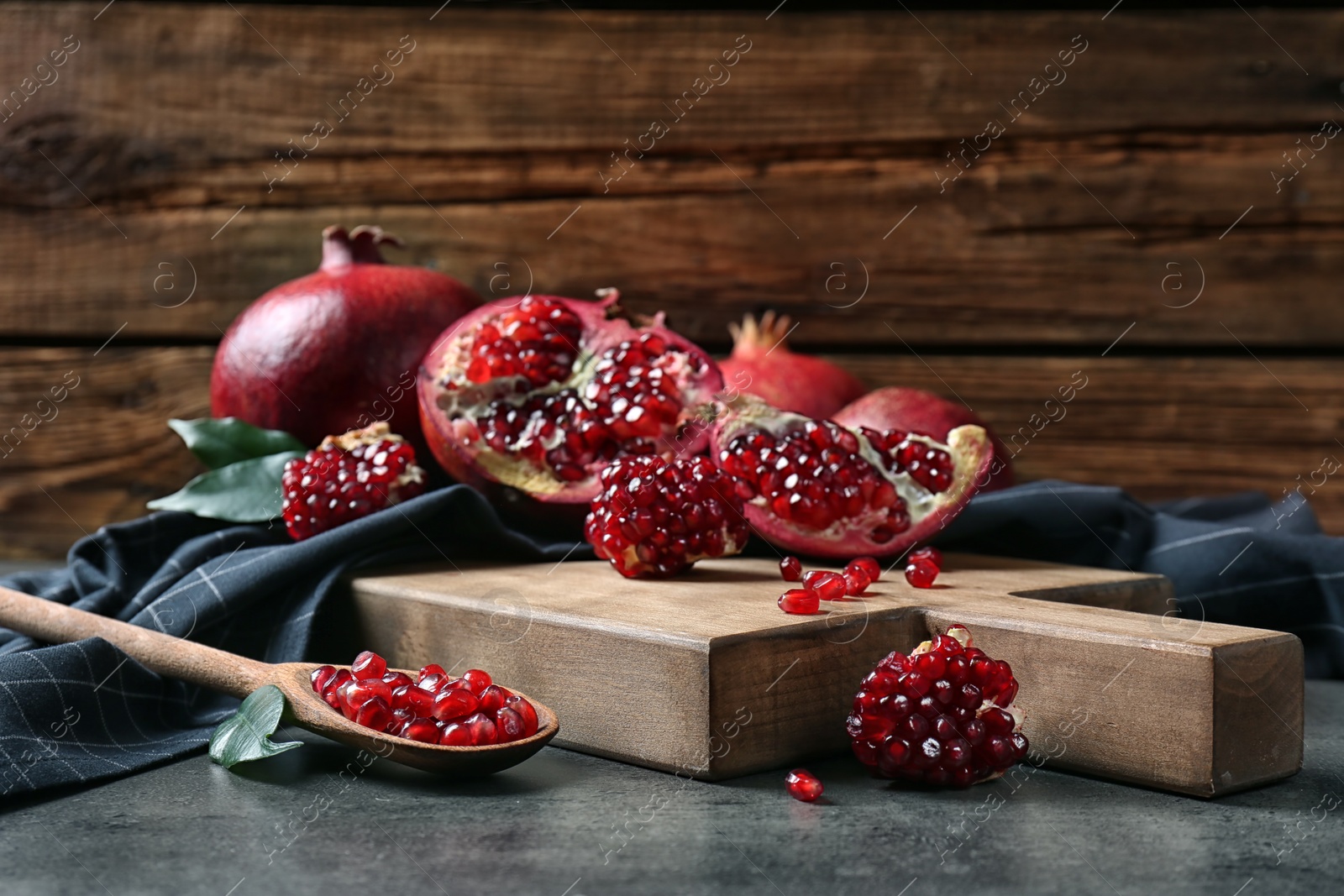 Photo of Ripe pomegranates and spoon with seeds on table against wooden background