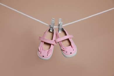 Photo of Cute small baby shoes hanging on washing line against brown background