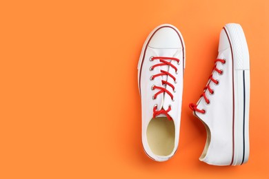 Photo of Pairtrendy sneakers on orange background, flat lay. Space for text