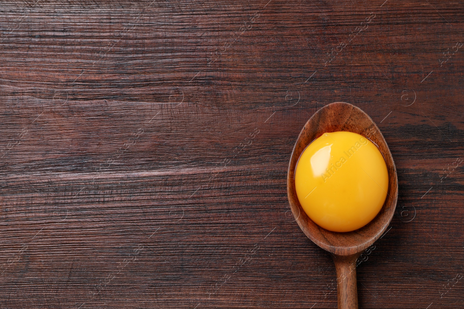 Photo of Spoon with raw egg yolk on wooden table, top view. Space for text