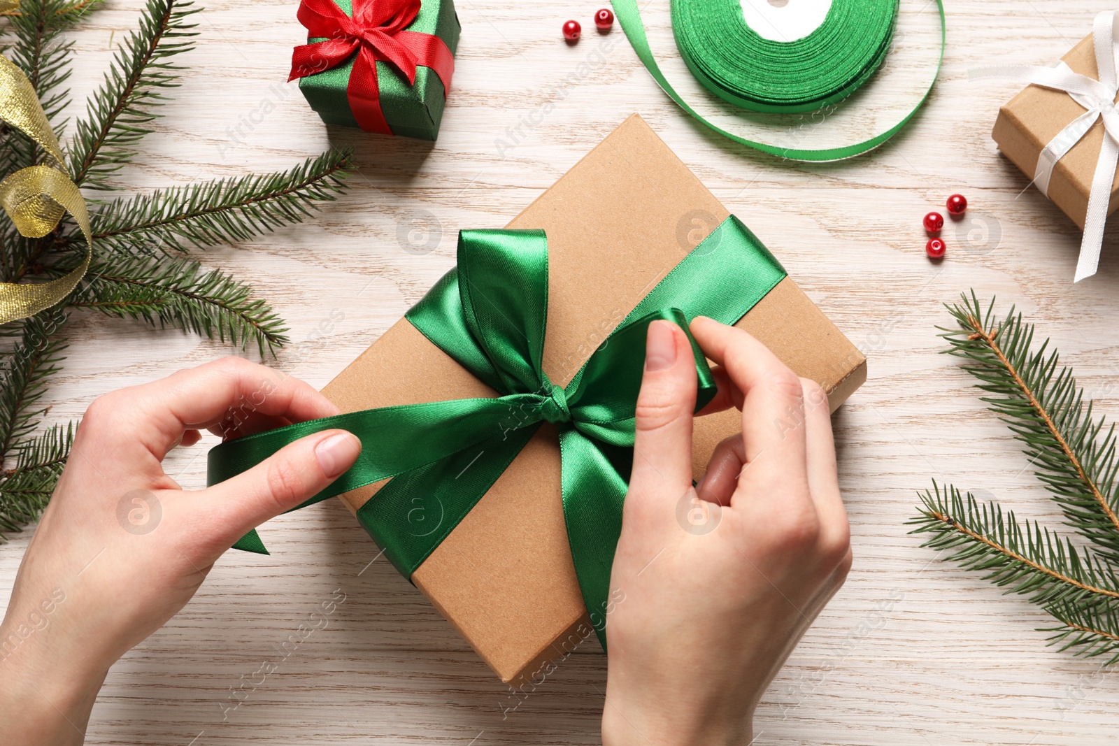 Photo of Woman decorating gift box at white wooden table, top view. Christmas present