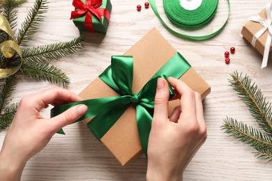 Photo of Woman decorating gift box at white wooden table, top view. Christmas present