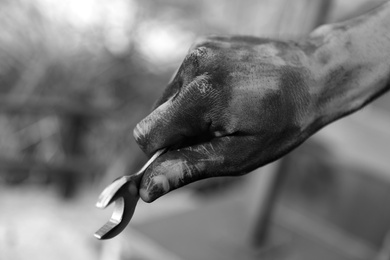 Photo of Dirty worker holding wrench on blurred background, closeup of hand. Black and white effect