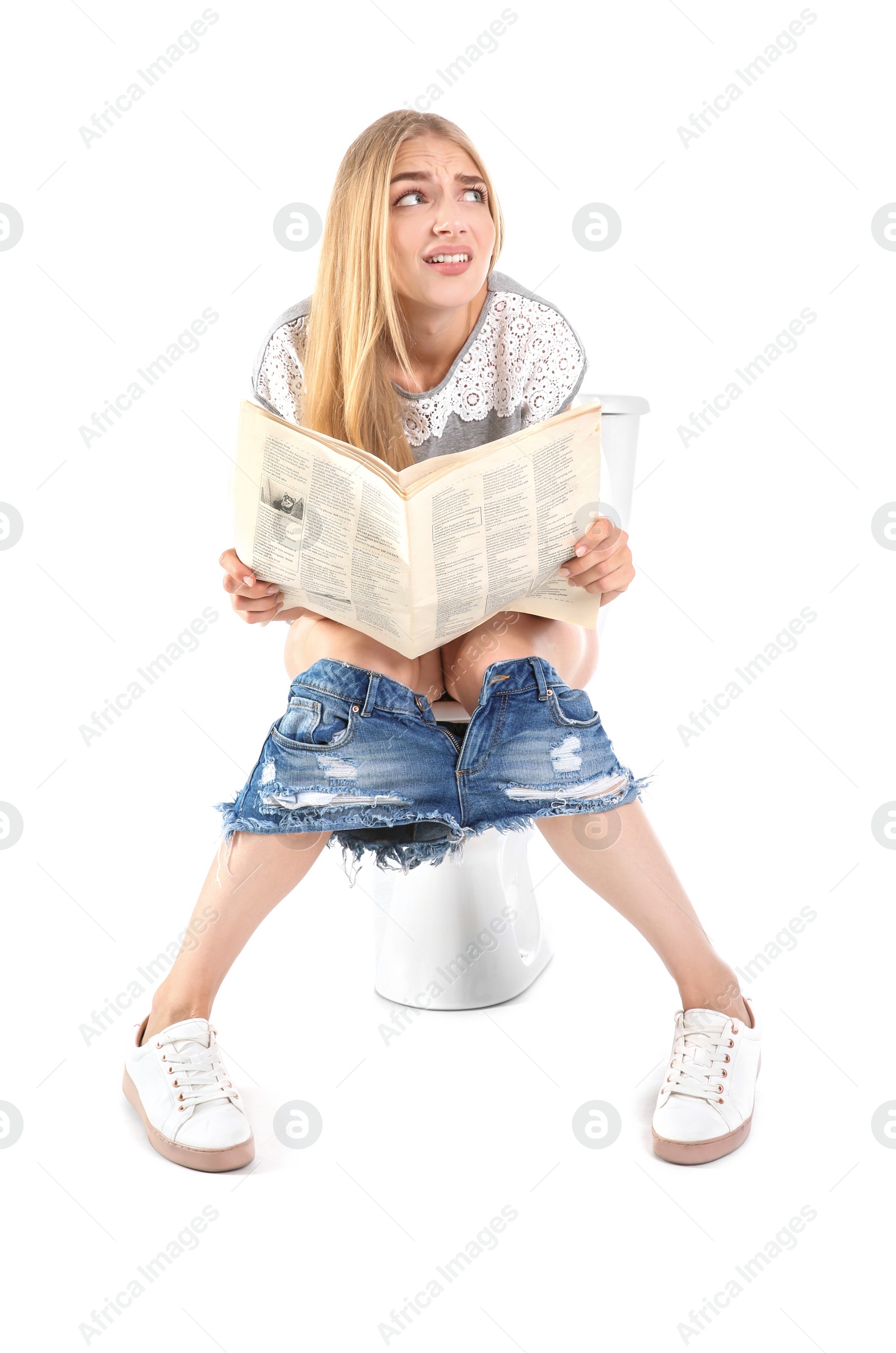 Photo of Young woman reading newspaper while sitting on toilet bowl. Isolated on white