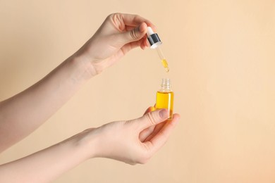 Photo of Woman holding bottle of cosmetic oil on beige background, closeup