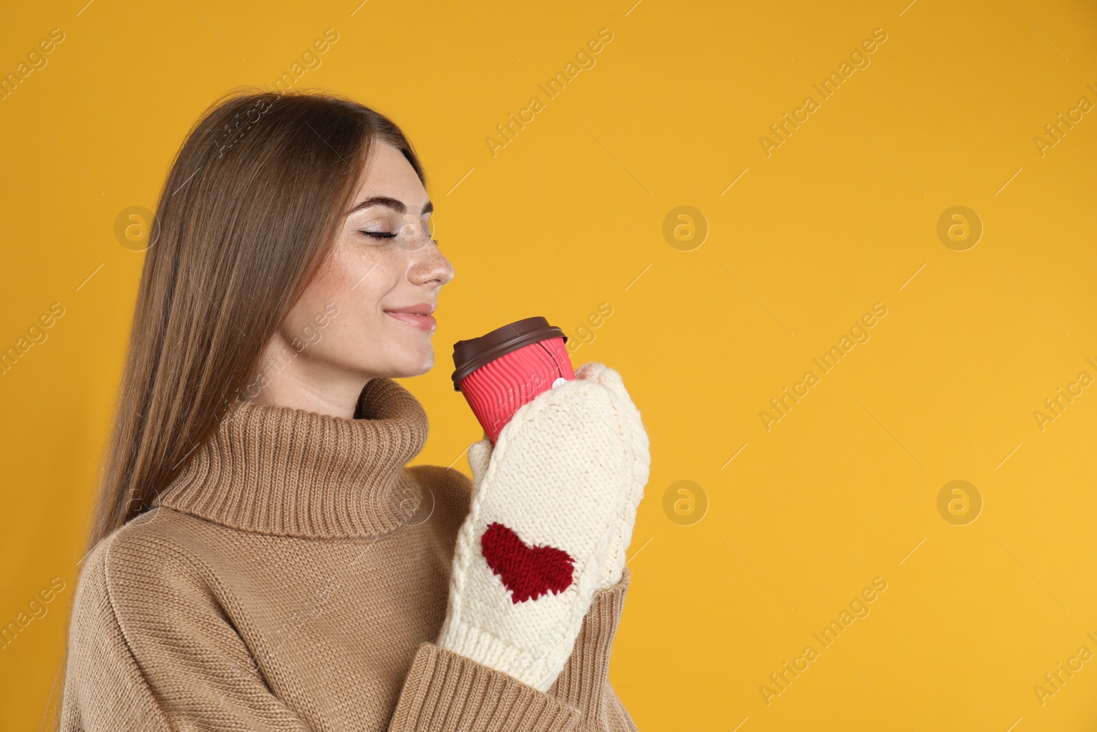 Photo of Happy beautiful woman with paper cup of mulled wine on yellow background. Space for text