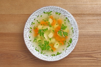 Photo of Bowl of fresh homemade soup to cure flu on wooden background, top view