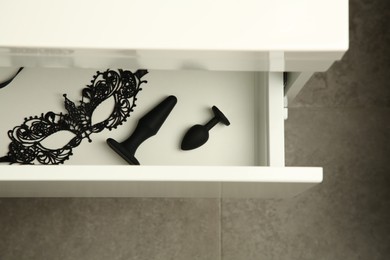 Black anal plugs and lace mask in drawer, top view. Sex toys