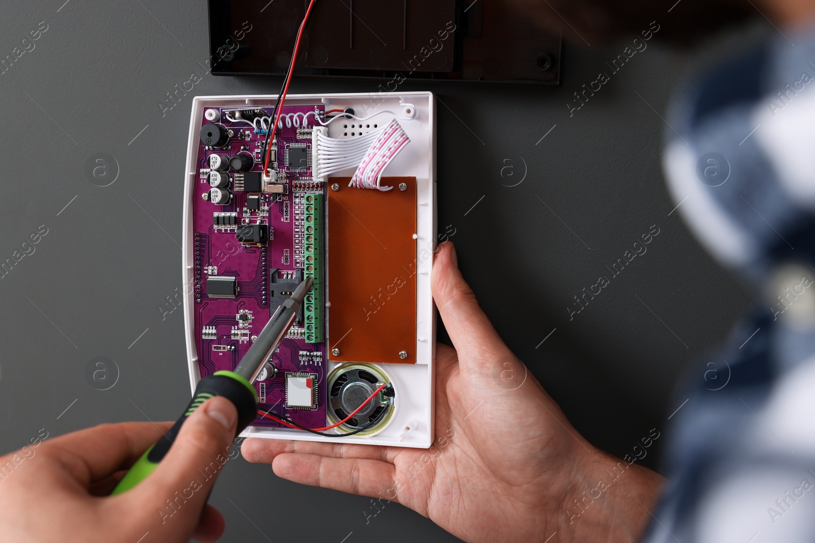 Photo of Man installing home security alarm system on gray wall, closeup