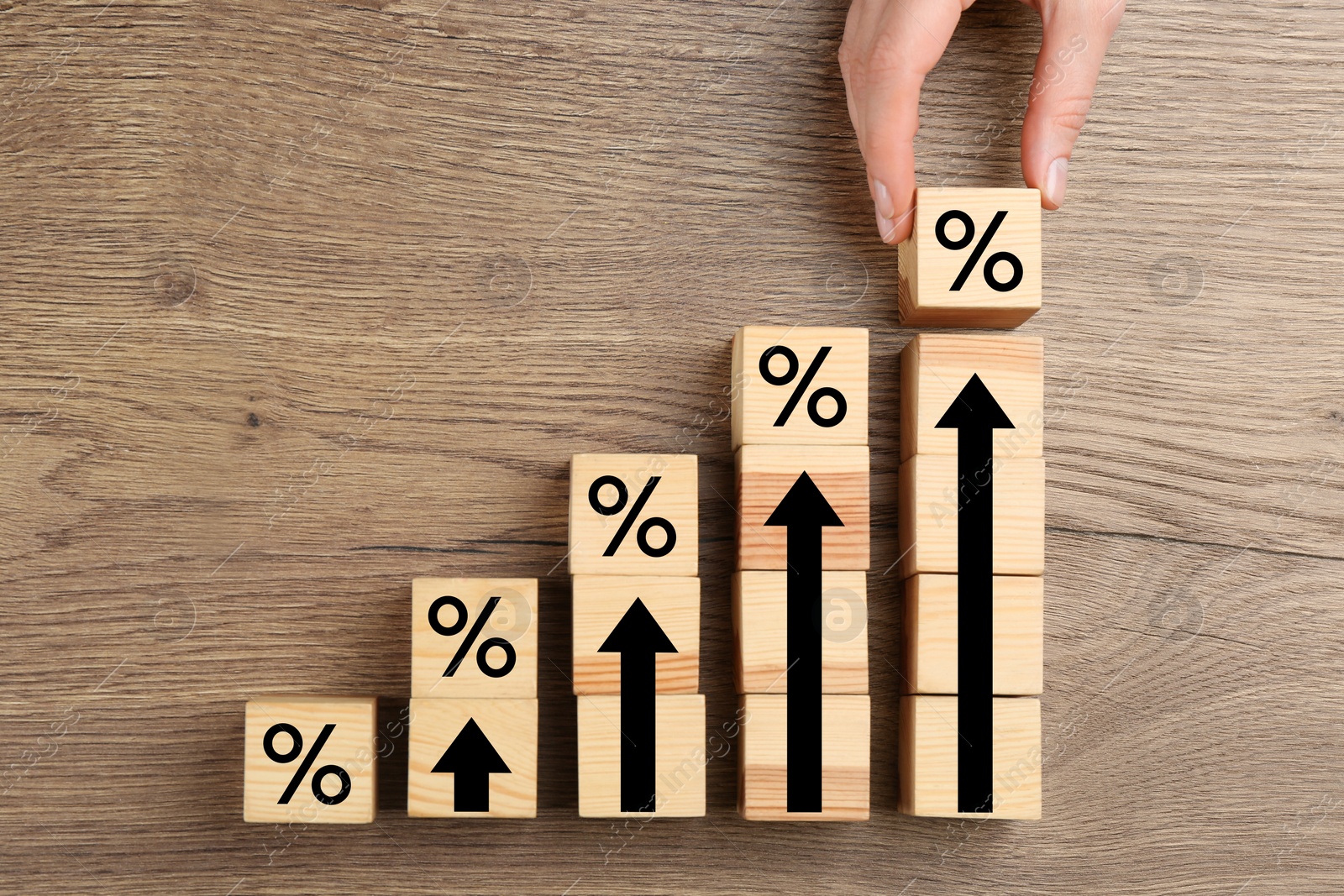 Image of Mortgage rate rising illustrated by upward arrows. Woman putting cube with percent sign near other ones on wooden table, top view