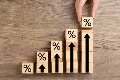 Image of Mortgage rate rising illustrated by upward arrows. Woman putting cube with percent sign near other ones on wooden table, top view