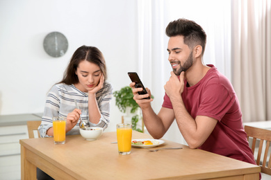 Photo of Young man preferring smartphone over his girlfriend at home