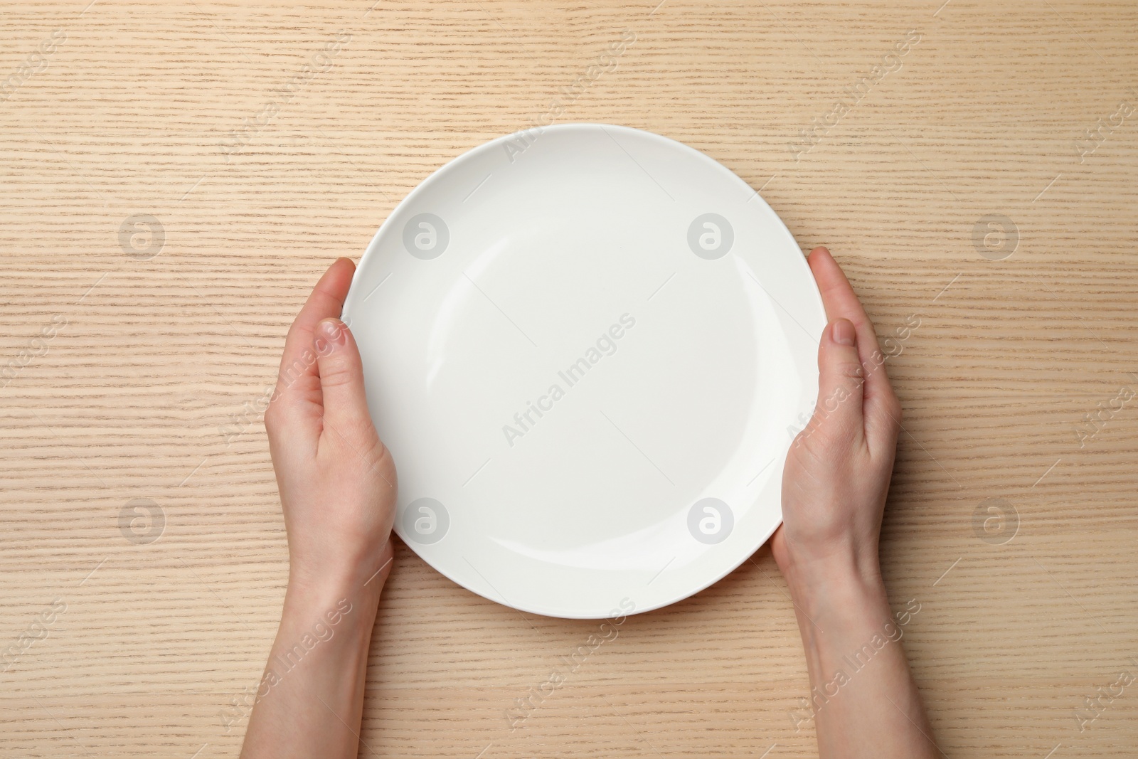 Photo of Woman with empty plate at wooden table, top view