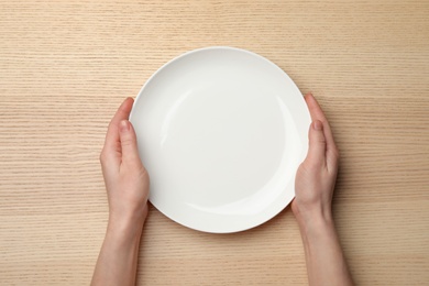 Woman with empty plate at wooden table, top view