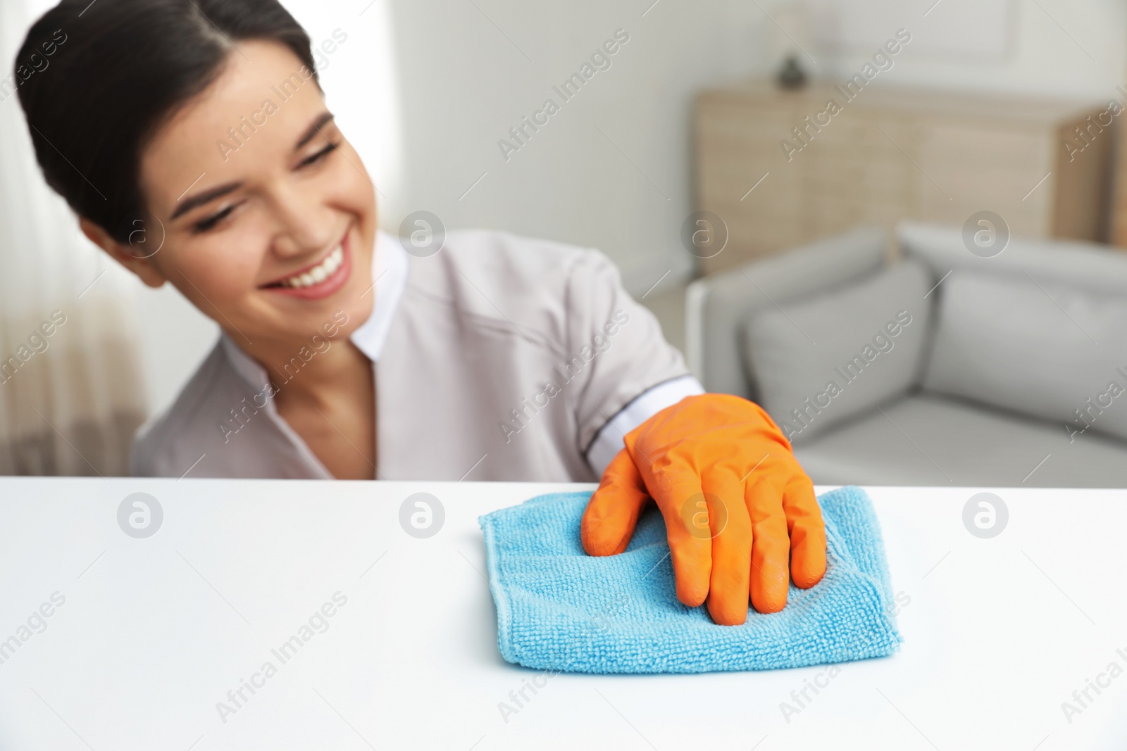 Photo of Young maid dusting furniture with rag in hotel room
