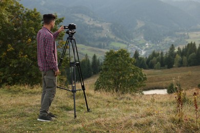 Photo of Man filming video with modern camera on tripod outdoors. Space for text