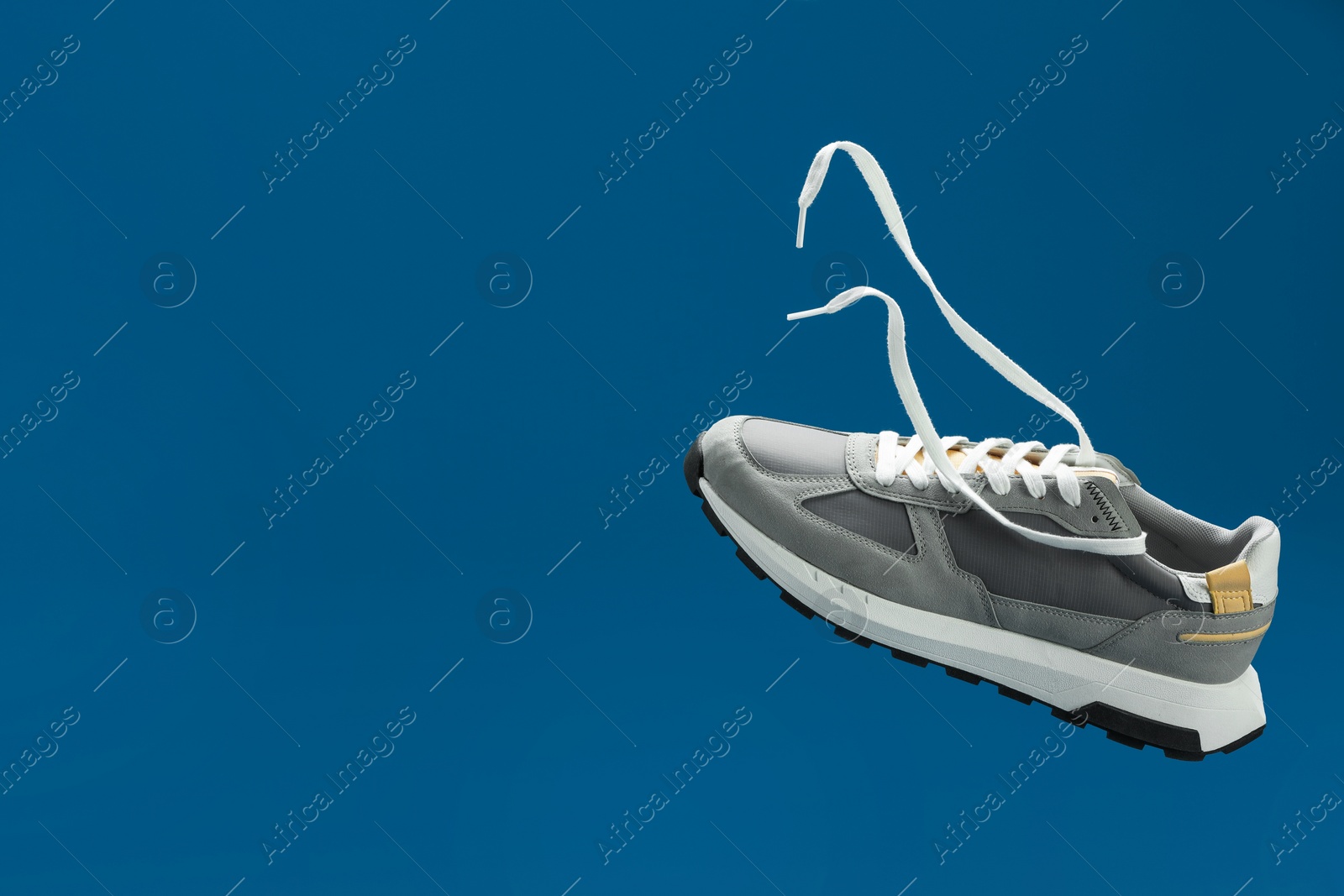 Photo of One stylish grey sneaker in air against blue background, space for text