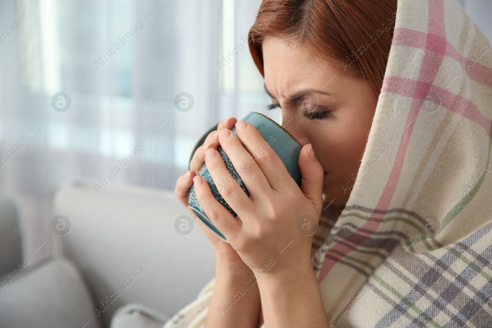 Photo of Sick woman wrapped in plaid with cup of hot drink at home. Influenza virus