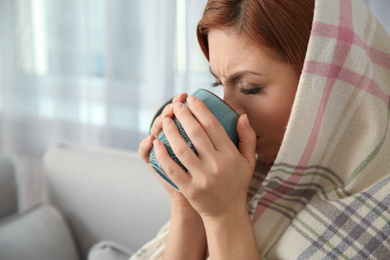 Photo of Sick woman wrapped in plaid with cup of hot drink at home. Influenza virus