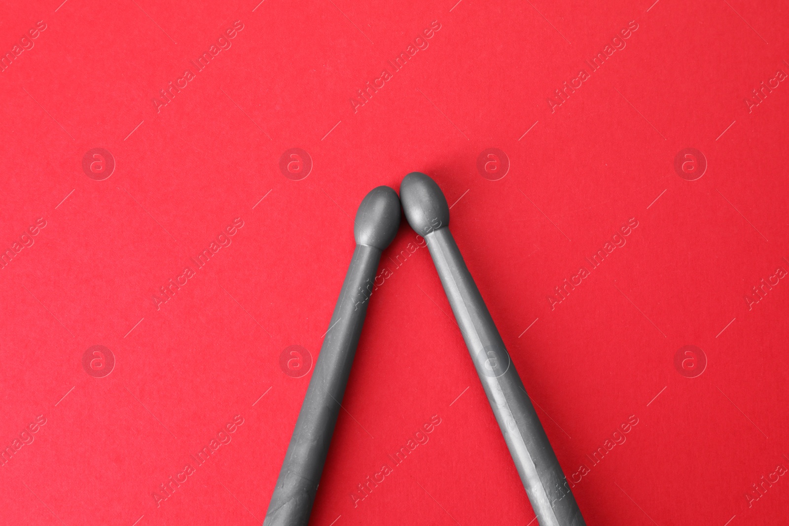 Photo of Two gray drum sticks on red background, top view