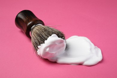 Photo of Brush with shaving foam on pink background, closeup