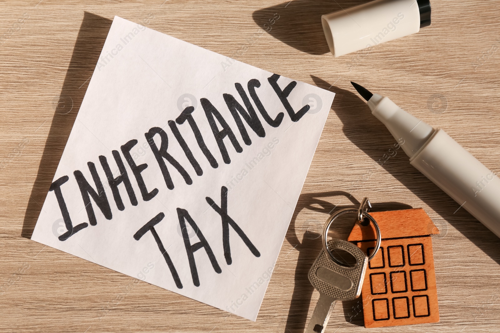 Photo of Inheritance Tax. Paper note, key with key chain in shape of house and marker on wooden table, flat lay