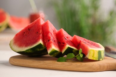 Photo of Slices of delicious ripe watermelon with mint on white wooden table indoors, closeup