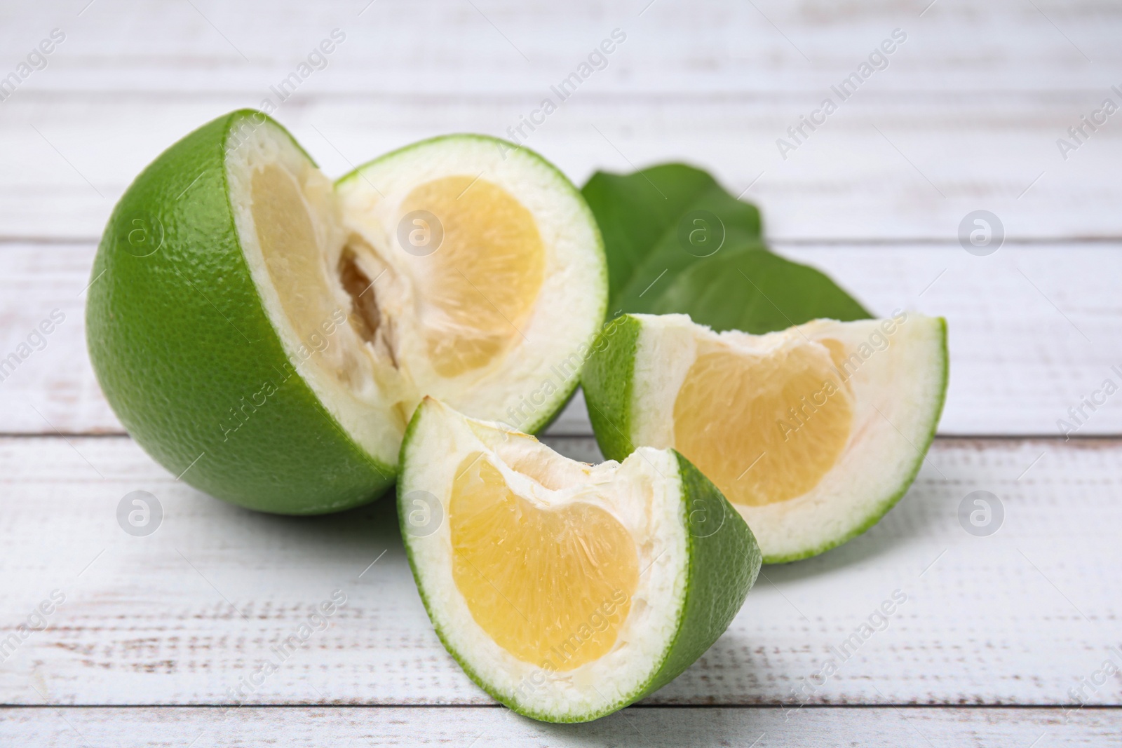 Photo of Cut fresh ripe sweetie fruit with green leaves on white wooden table, closeup