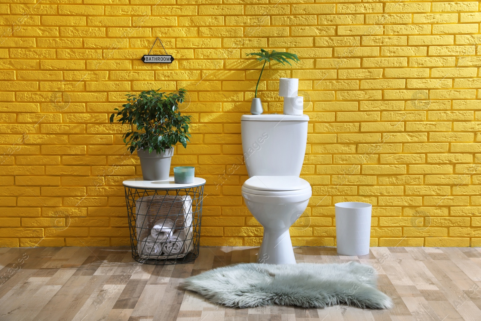 Photo of Stylish bathroom with toilet bowl, green plants and decor elements near yellow brick wall. Interior design