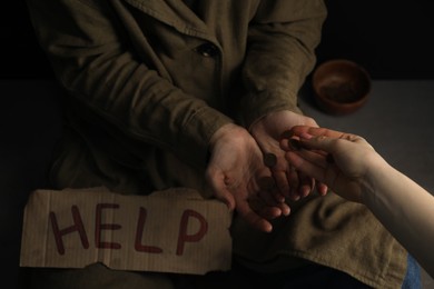 Photo of Woman giving coins to homeless with help sign, closeup. Charity and donation