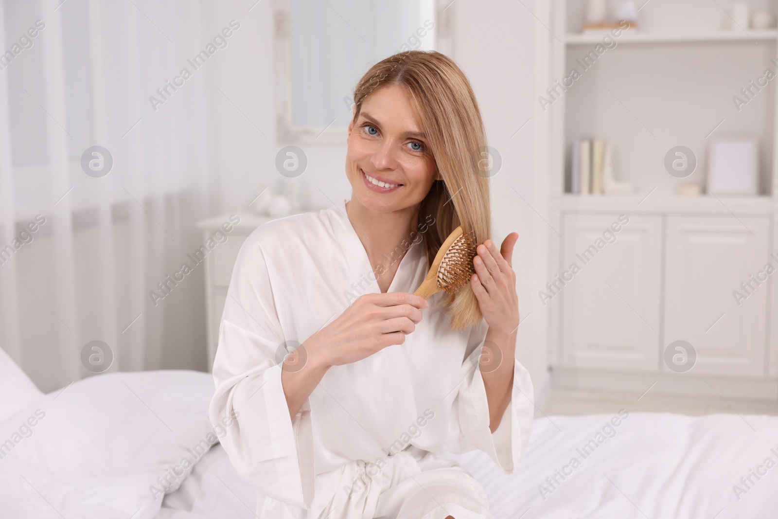 Photo of Beautiful woman brushing her hair on bed in room