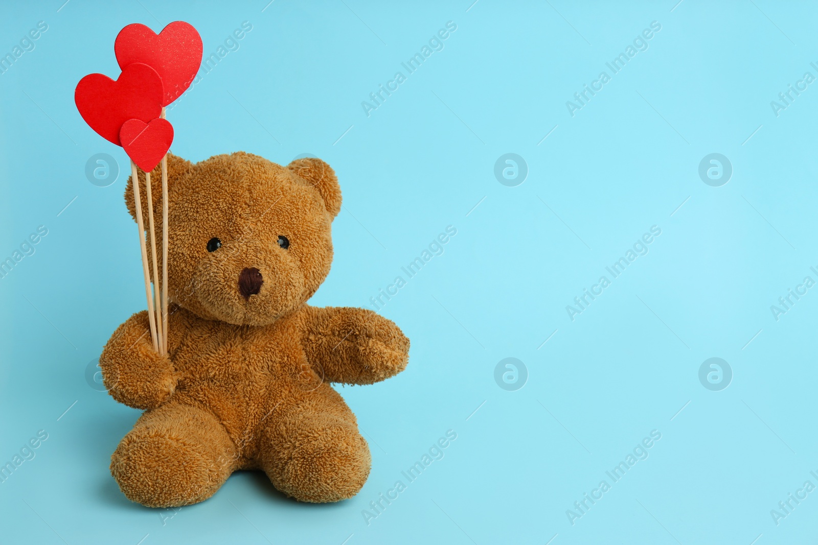 Photo of Cute teddy bear with red hearts on light blue background, space for text. Valentine's day celebration
