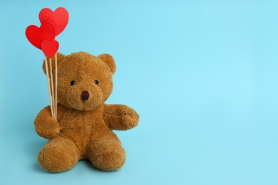 Photo of Cute teddy bear with red hearts on light blue background, space for text. Valentine's day celebration